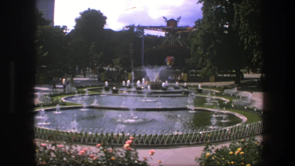 1975 Copenhagen park fountain view with foreground flowers, low fencing, circular basins, water jets, trees, paths, and distant visitors.