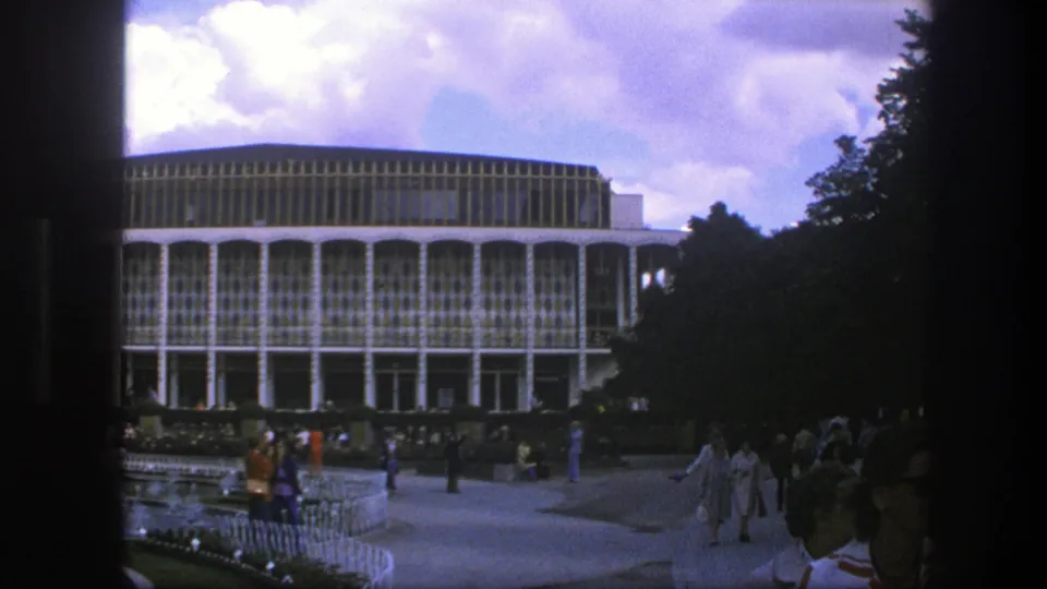 1975 Copenhagen home-movie view of a large modernist exterior, visitors, landscaping, and a shaded walkway area.