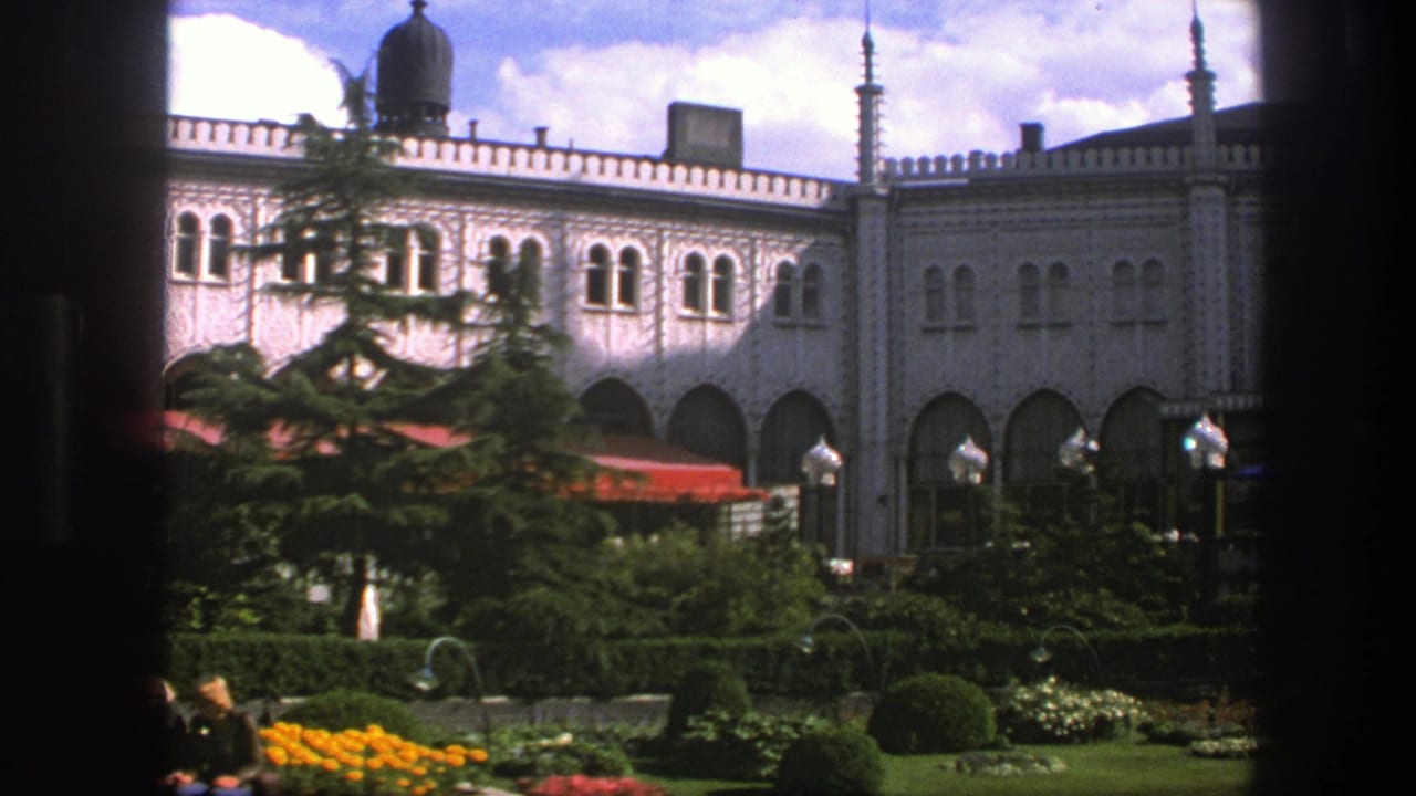 Ornate pale building behind a garden, seen through dark window framing.
