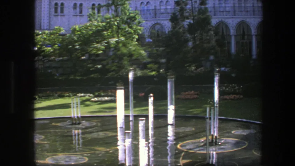 1975 Copenhagen 8mm view of a formal reflecting pool with white vertical columns, trees, lawn, and an ornate pale building in back.