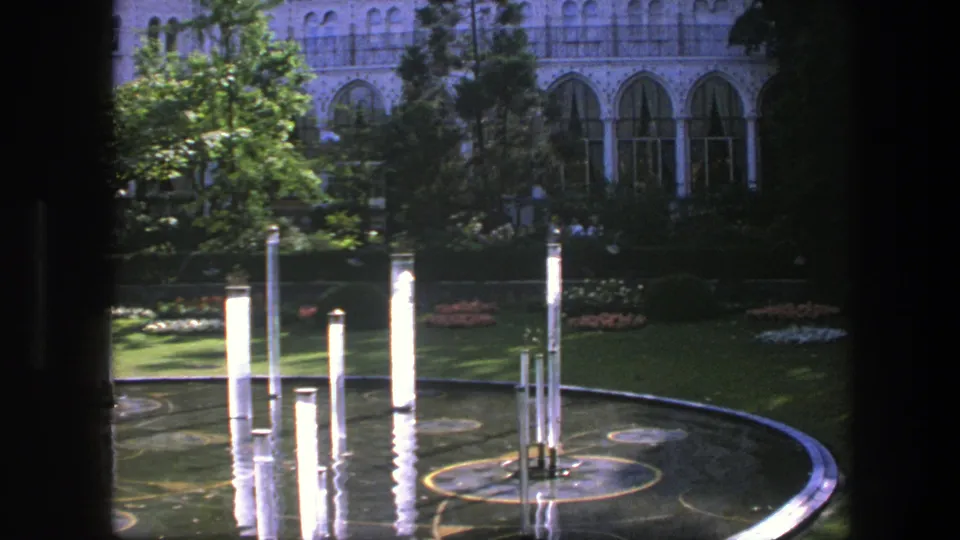 A 1975 Copenhagen frame shows bright columns reflected in a circular pool, with clipped grass, trees, and arched windows beyond.