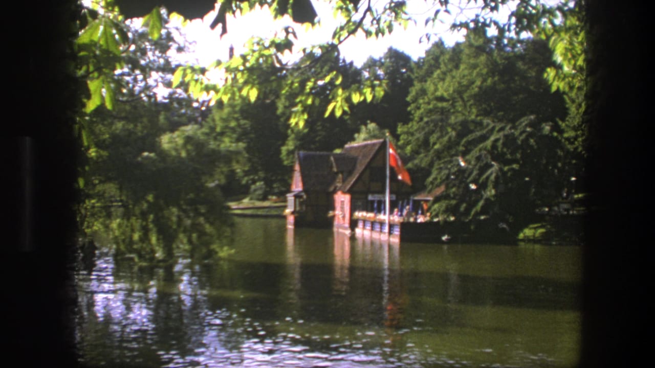 Boathouse across a lake framed by leaves and trees.