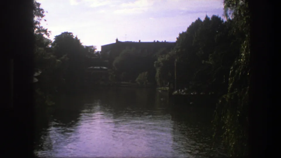 1975 Copenhagen frame with a darker exposure across the lagoon, silhouetted trees, willow foliage, and buildings beyond the water.