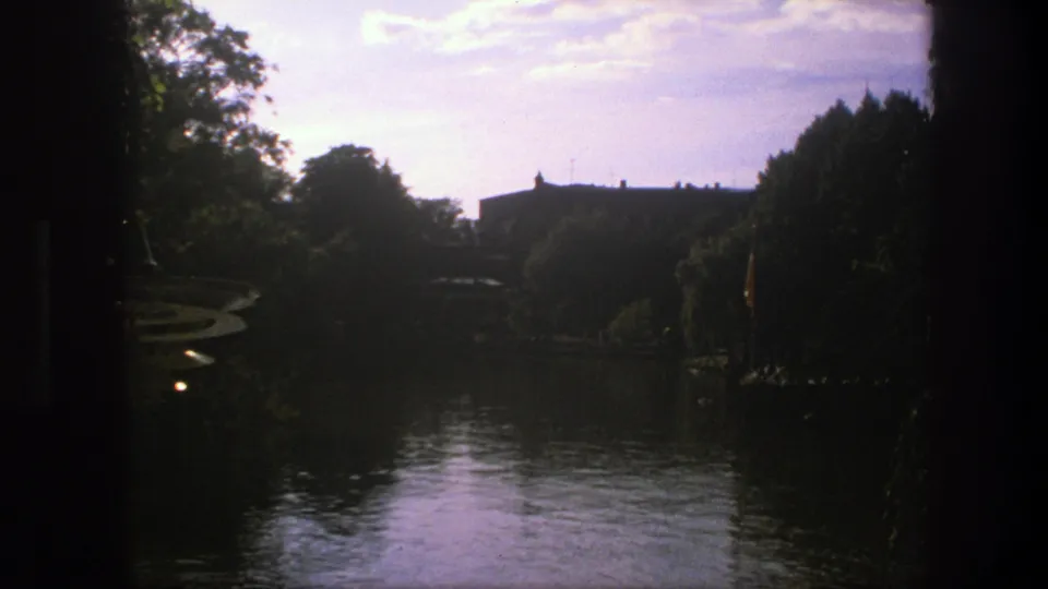 1975 Copenhagen frame of reflective water, tree-lined banks, and a distant building softened by 8mm exposure.
