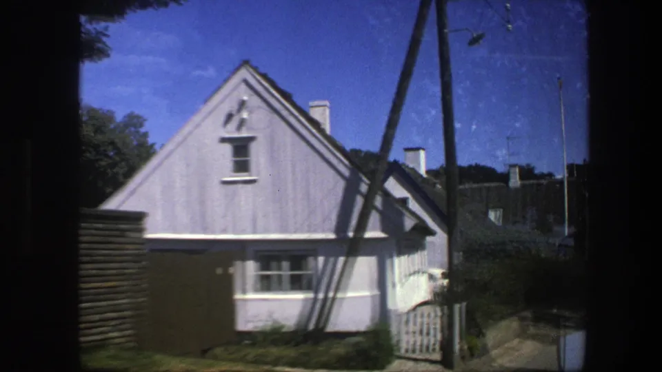 1975 Copenhagen frame centered on a pale gabled house with a small gate, fence, utility poles, and neighboring roofs.