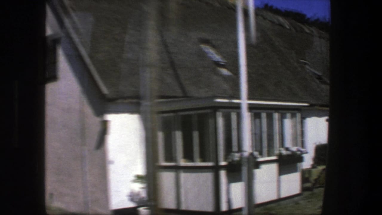 Copenhagen-area 1975 travel footage frames a thatched cottage corner with white walls, dark framing, and small windows.
