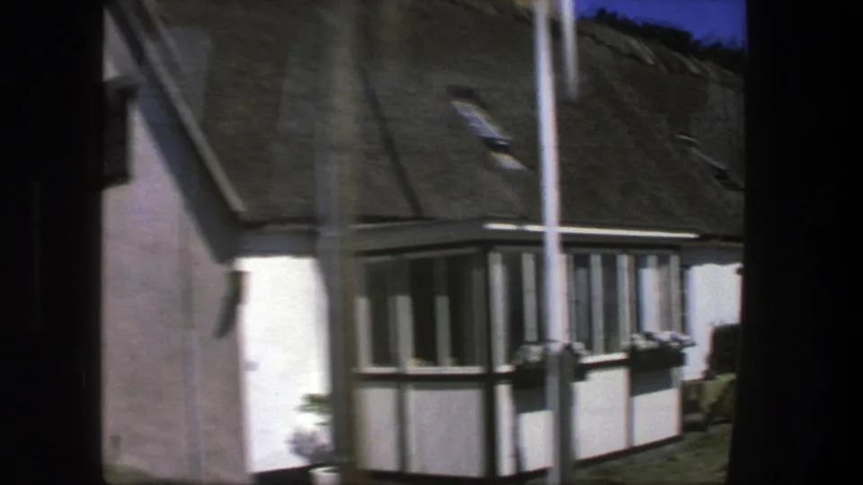 Copenhagen-area 1975 travel footage frames a thatched cottage corner with white walls, dark framing, and small windows.