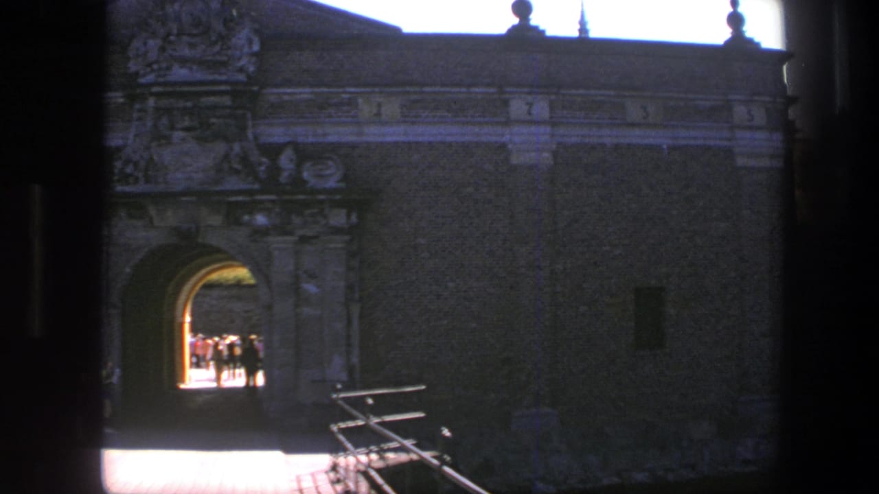 1975 Copenhagen 8mm frame looking from shade toward a historic fortress arch where tourists stand in the sunlit passage.