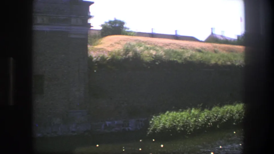 A later frame shows the Copenhagen fortress wall edge with greenery, a moat-side foreground, and a sunlit rampart beyond.