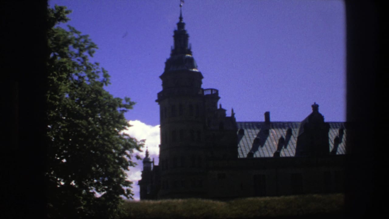 1975 Copenhagen 8mm frame with the historic landmark tower and roofline silhouetted against blue sky beside leafy trees.