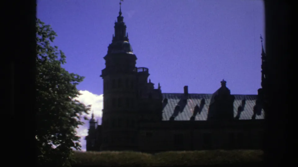 1975 Copenhagen home-movie frame showing a darker, closer view of the landmark tower, roofline, trees and grass.