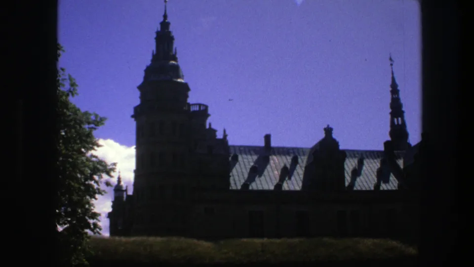 1975 Copenhagen 8mm frame showing the landmark tower, long roofline and a narrow spire at the right edge under blue sky.