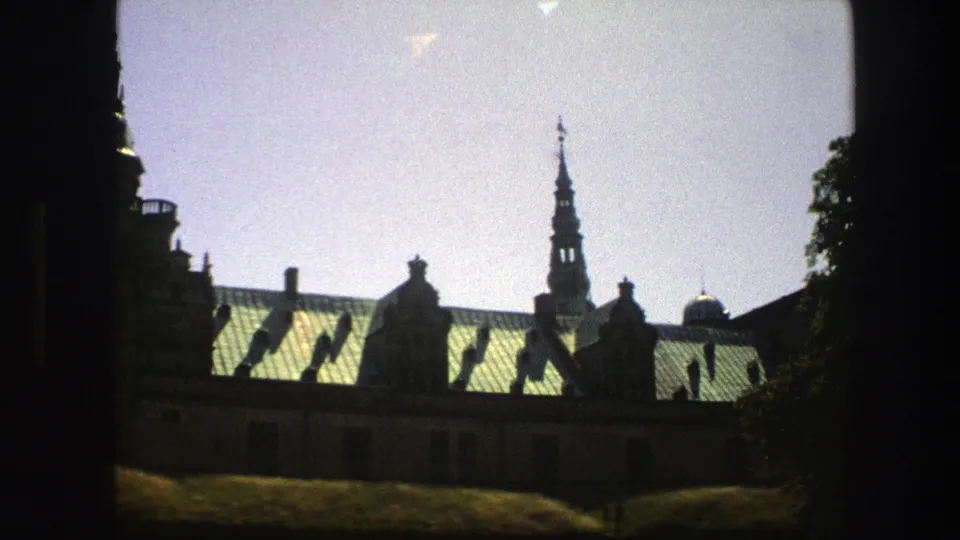 Copenhagen historic church roofline and spire in a 1975 8mm frame, with tree foliage at the right edge.