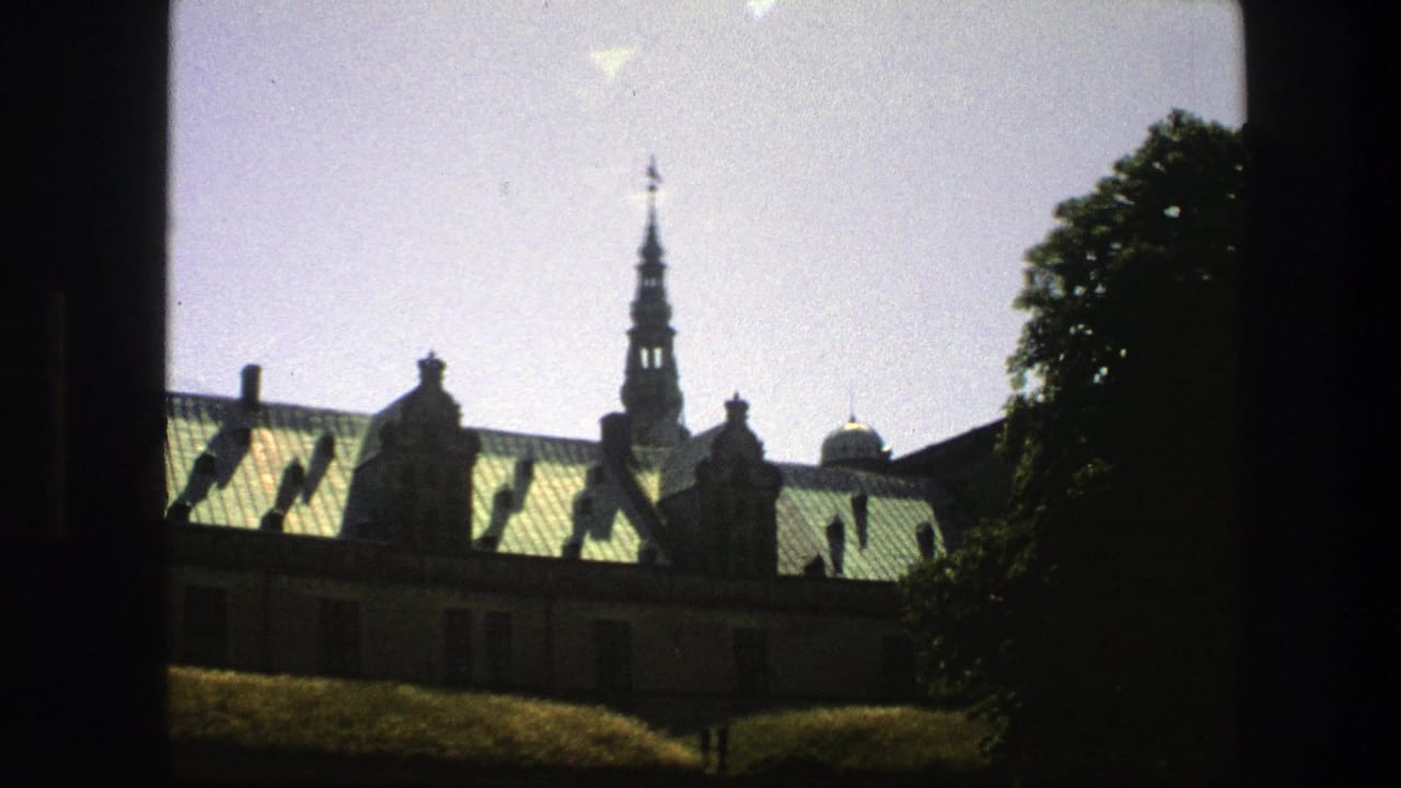 1975 Copenhagen frame with a green-roofed historic building, narrow spire, trees, pale sky, and dark border from the shooting position.