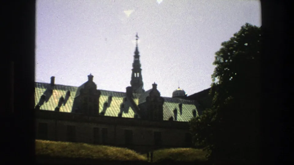 1975 Copenhagen frame with a green-roofed historic building, narrow spire, trees, pale sky, and dark border from the shooting position.