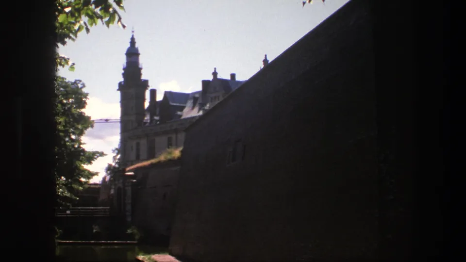 1975 Copenhagen frame showing a long brick wall, a towered historic building, roof forms, trees, and heavy foreground shadow.