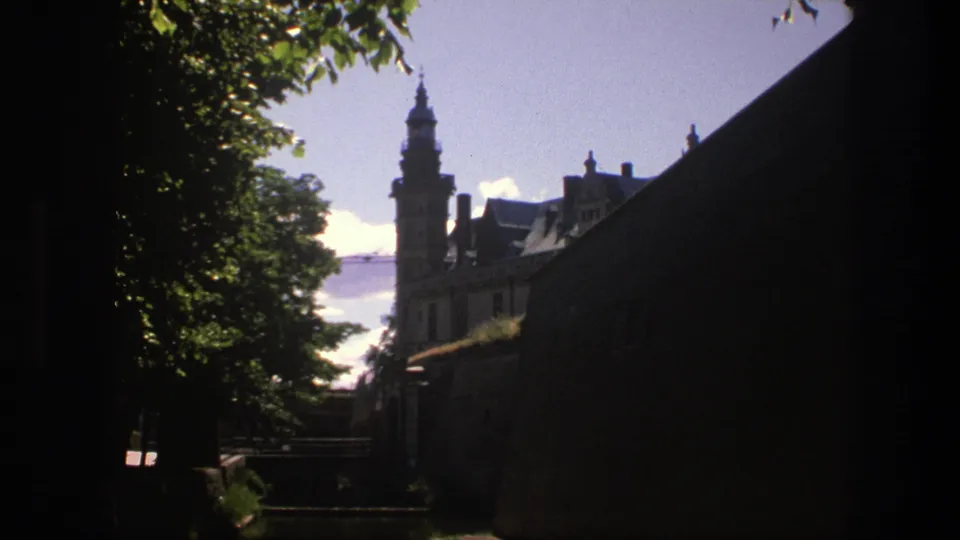 Copenhagen travel footage frame with trees and masonry enclosing a distant castle tower in bright daylight.