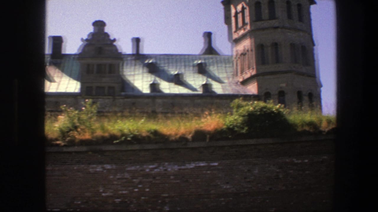 1975 Copenhagen 8mm frame showing an ornate historic building roof, tower, chimneys, grass, and brickwork through a dark opening.