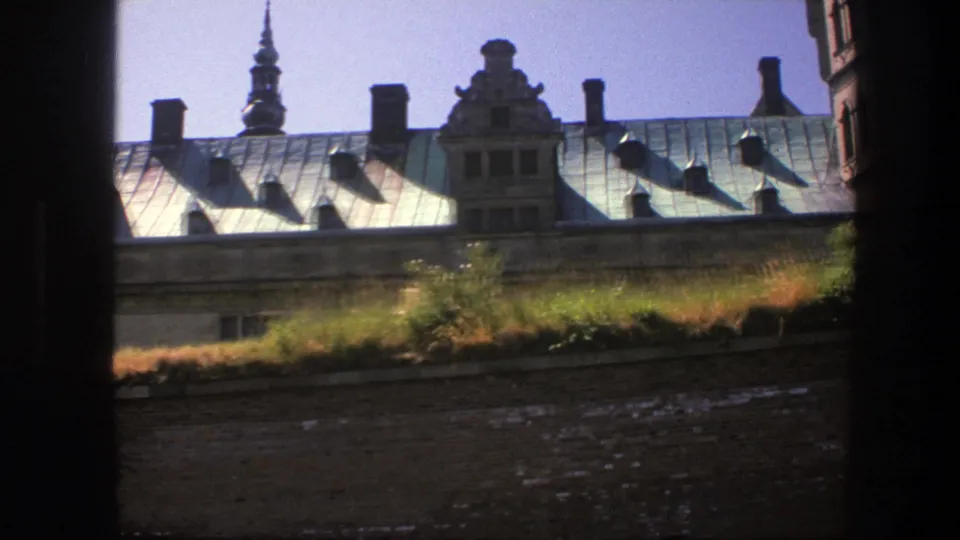 1975 Copenhagen 8mm view of a historic roofline with ornate gables, chimneys, and a tower spire seen from behind a dark frame.