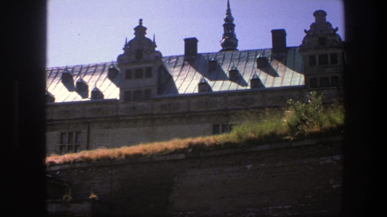 1975 Copenhagen travel footage frame of a sunlit metal roof with decorative gables, chimneys, and a spire beyond dark side framing.