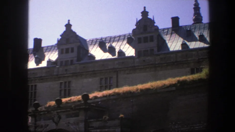 1975 Copenhagen 8mm frame with angled rooftop composition, decorative gables, chimneys, stone facade, and dark frame edges.