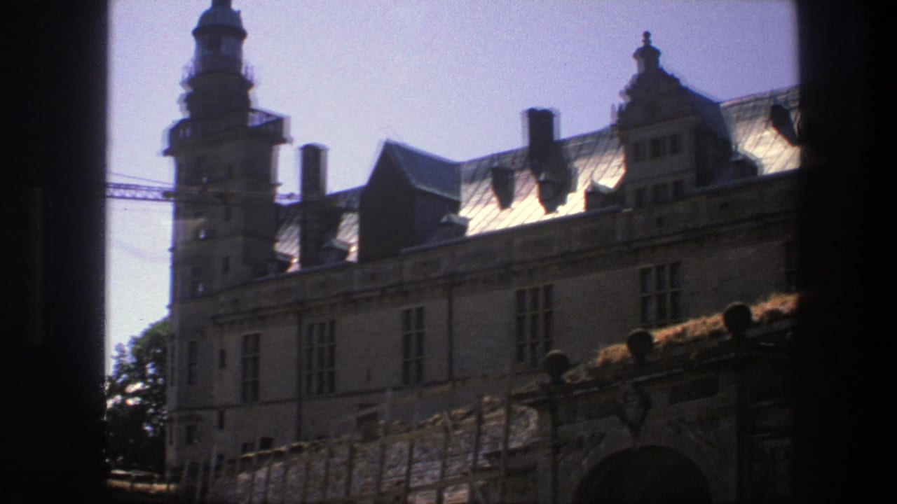 Historic castle facade and tower seen through a dark foreground frame with crane behind.