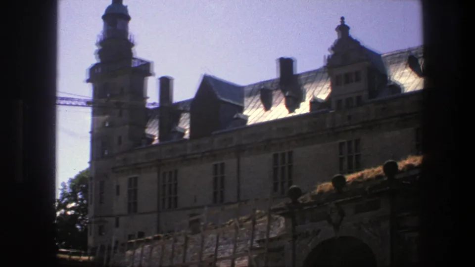 1975 Copenhagen home-movie frame showing a castle facade, tower, roofline, chimneys, and construction crane through a dark opening.