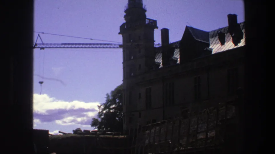 Late frame from the 1975 Copenhagen clip showing the castle tower and roofline in shadow with a crane, trees, and clouds behind.