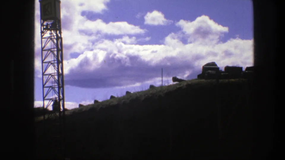 1975 Copenhagen 8mm frame showing a silhouetted lattice tower and dark ridge against a vivid cloudy sky.