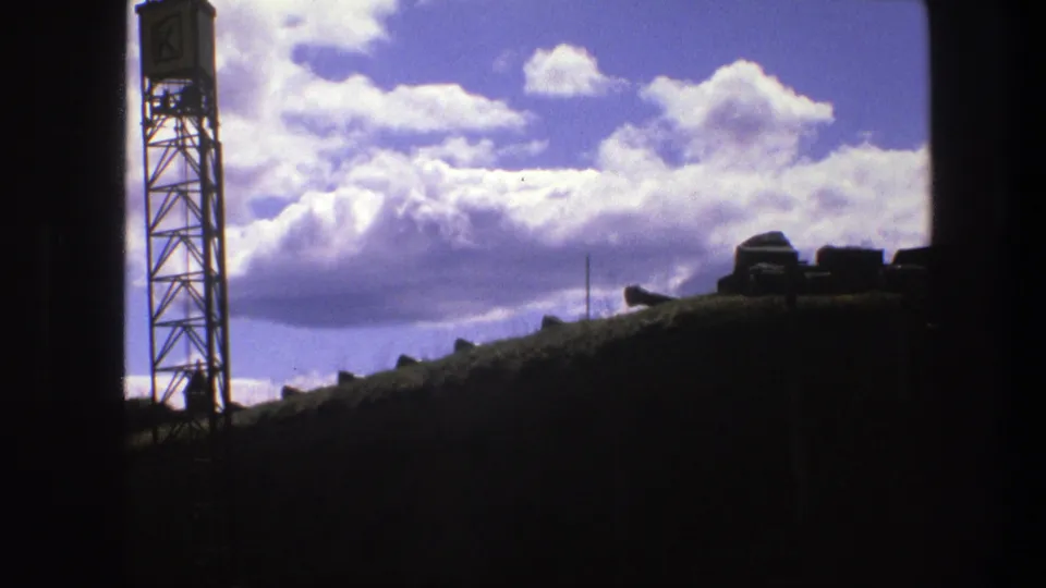 1975 Copenhagen home-movie frame with a tower silhouette, shadowed foreground, and bright cloud banks.