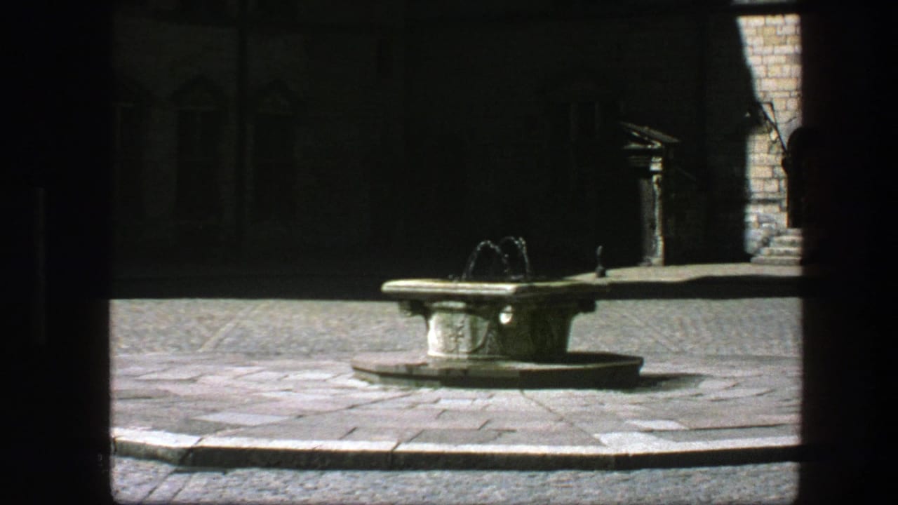 1975 Copenhagen home-movie frame showing a stone fountain flowing in a sunlit courtyard seen from deep shade.