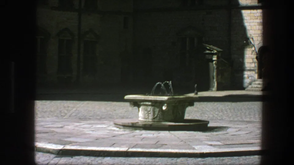 Stone fountain in a Copenhagen courtyard, with old masonry walls and windows visible beyond the shaded foreground.