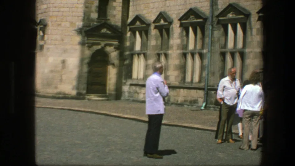 Visitors in 1970s casual clothing stand near a historic Copenhagen building facade with tall windows and a doorway.