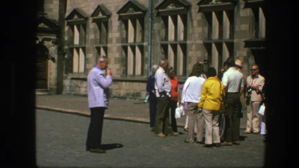 1975 Copenhagen frame of adults in casual clothing gathered near a stone building, with faces visible and no signage apparent.