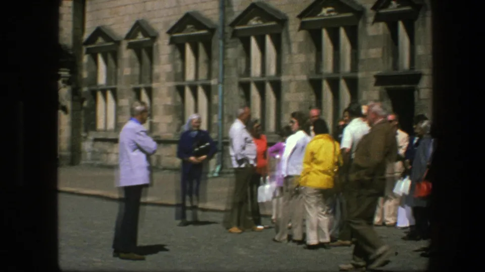 1975 Copenhagen home-movie frame showing a loose civilian gathering outside a historic-looking stone building in daylight.