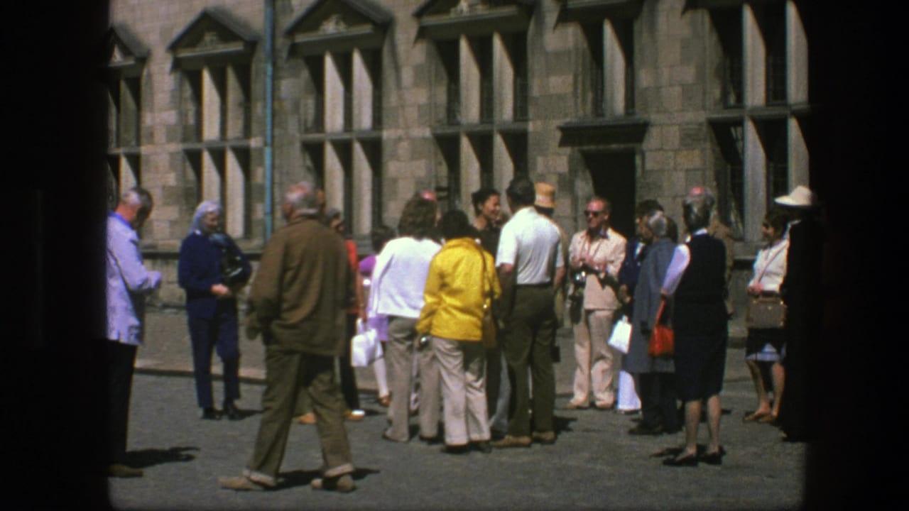 Tourists gather in a courtyard before a stone building with tall windows.