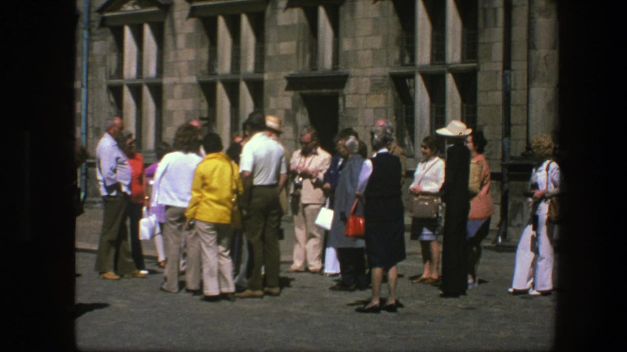 Group of visitors stands near a stone wall, with hats, bags, and cameras visible.