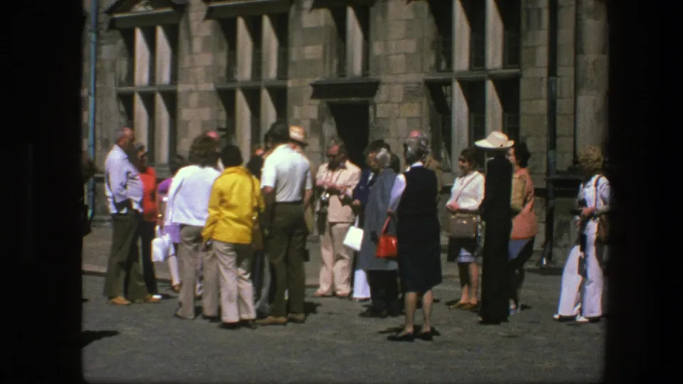 Tourists in 1970s attire gather in a Copenhagen courtyard beside a historic stone facade.