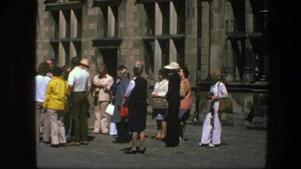 1975 Copenhagen frame with tourists moving and standing outside a stone building during a sightseeing stop.