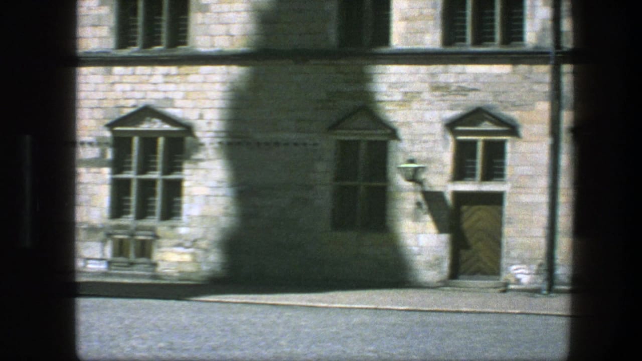 Stone building facade with mullioned windows, wooden door, street lamp, and dark film borders.