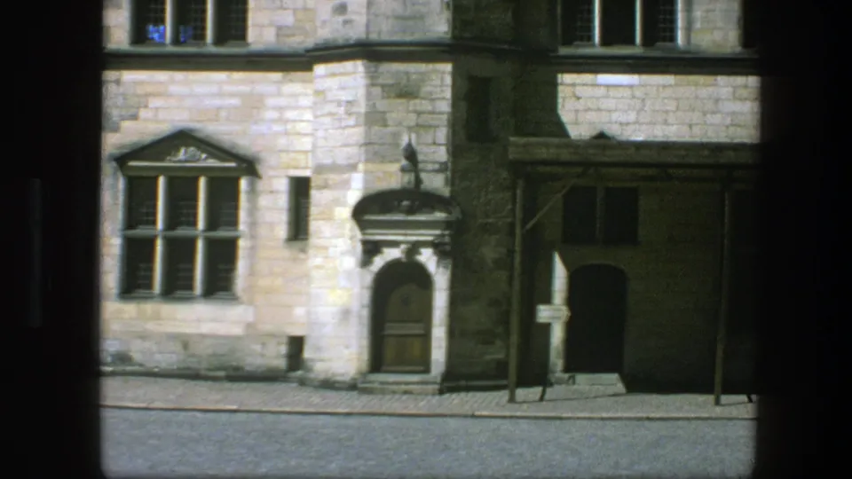1975 Copenhagen exterior view showing a stone building corner, arched wooden doorway, mullioned windows, shaded side entrance, and paved street.