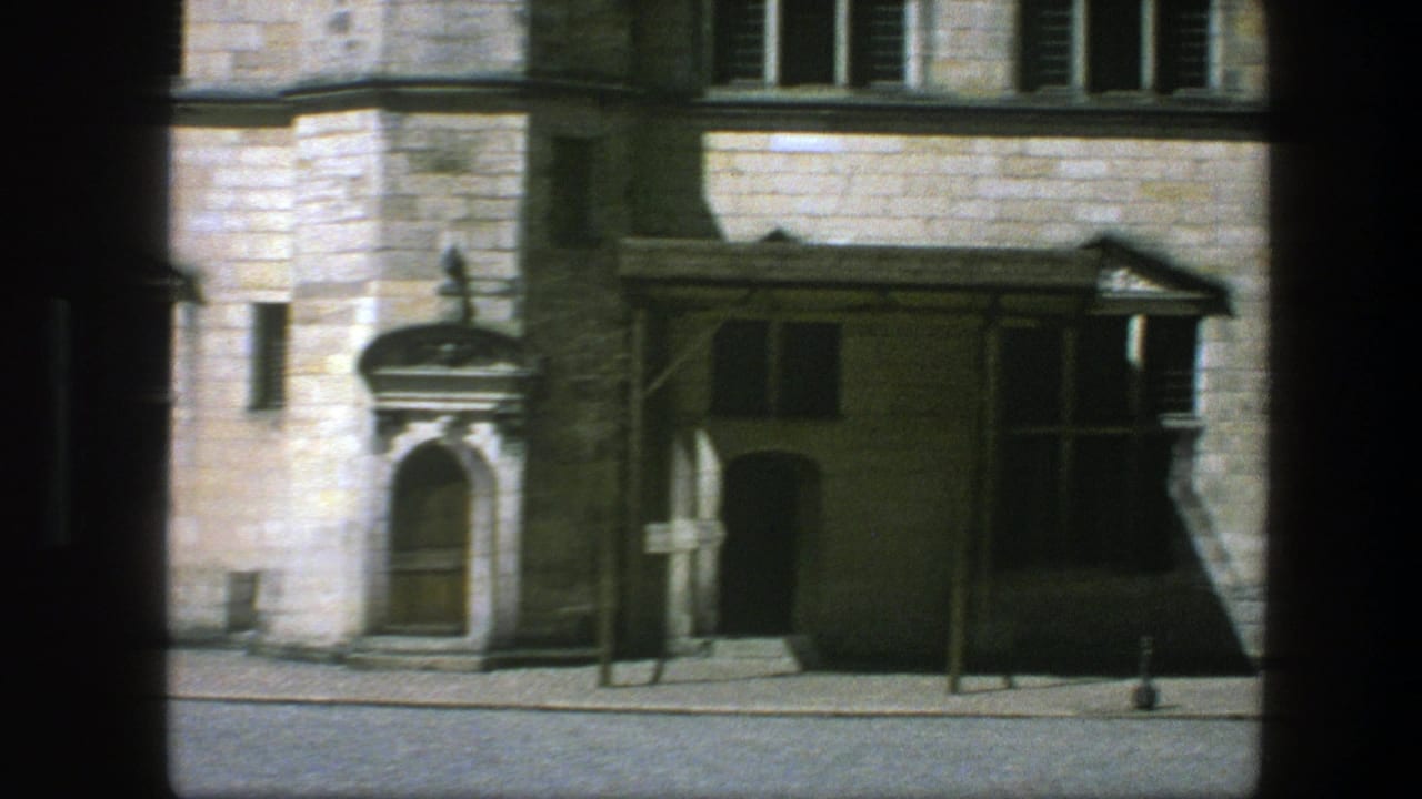 Stone building frontage with arched doorway, windows, cobblestone street, and dark film-frame edges.