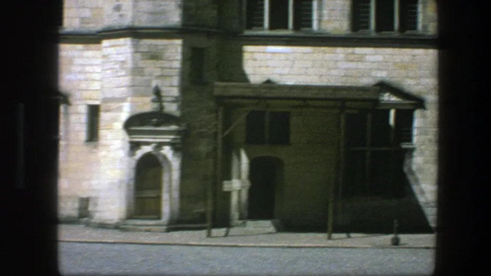 1975 Copenhagen street view showing a pale stone facade, arched entry, mullioned windows, and cobblestone pavement.