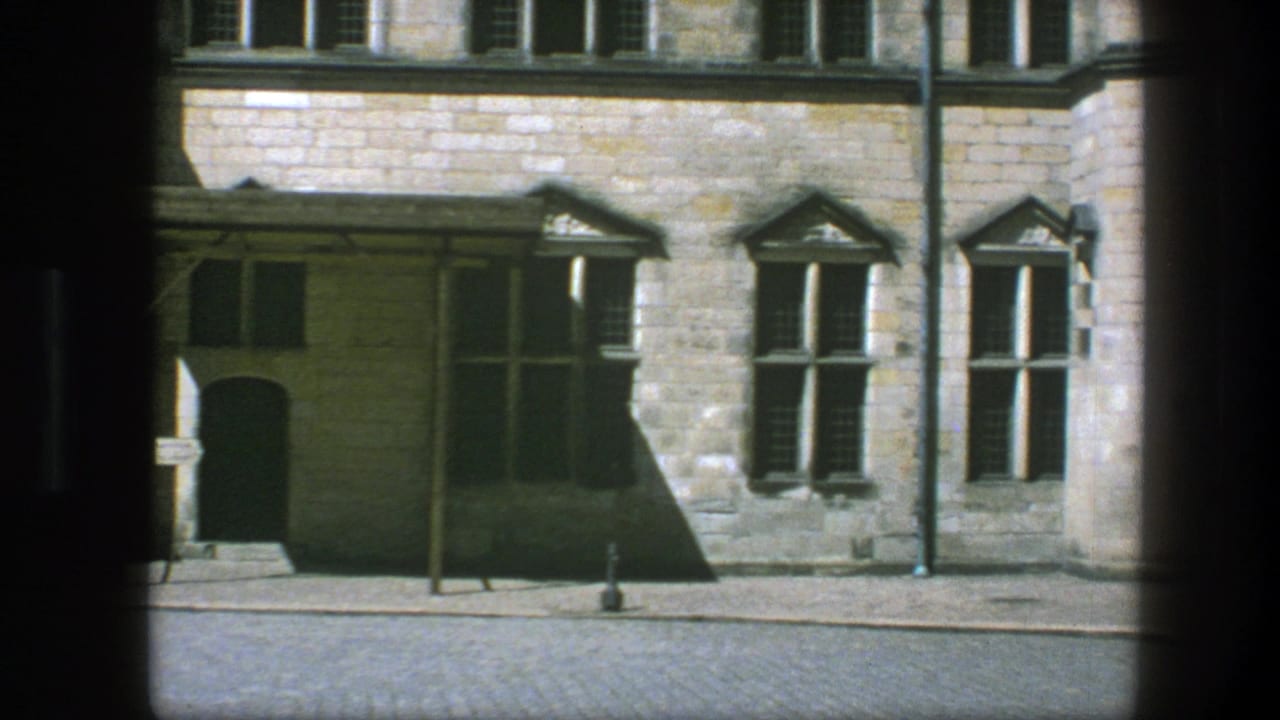 Historic stone facade with shuttered windows, recessed doorway, cobblestones, and street posts.