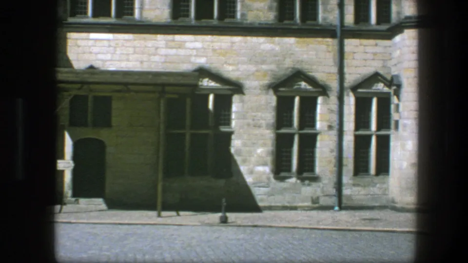 1975 Copenhagen facade detail with tall windows, a shadowed arched doorway, cobblestone paving, and sparse street fixtures.