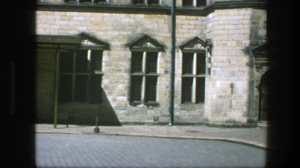 1975 Copenhagen street frame showing a stone corner, mullioned windows, a drainpipe, bollard, and empty cobblestone roadway.