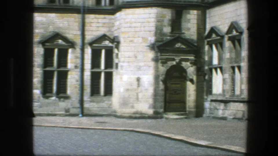 1975 Copenhagen street view with an arched doorway, pale masonry, tall windows, drainpipe, and empty cobblestone street.