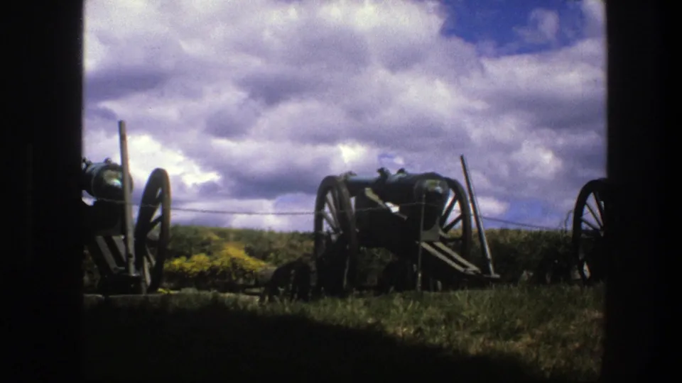 1975 Copenhagen frame showing cannons on a fortification-like grassy area beneath a cloud-filled sky.