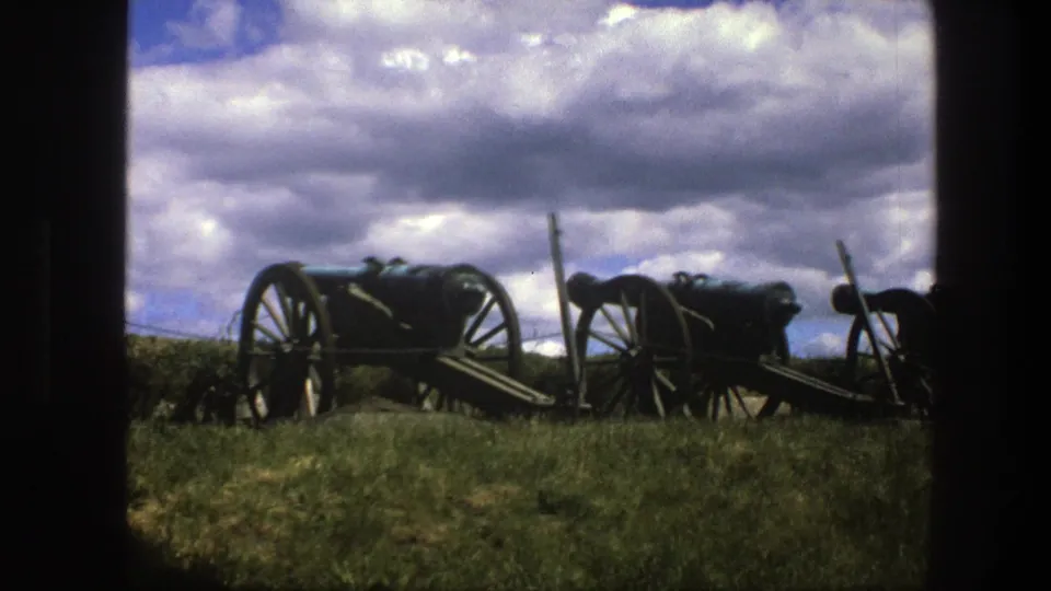 1975 Copenhagen 8mm frame showing a row of antique cannons on wooden-spoked carriages in a grassy field under bright clouds.