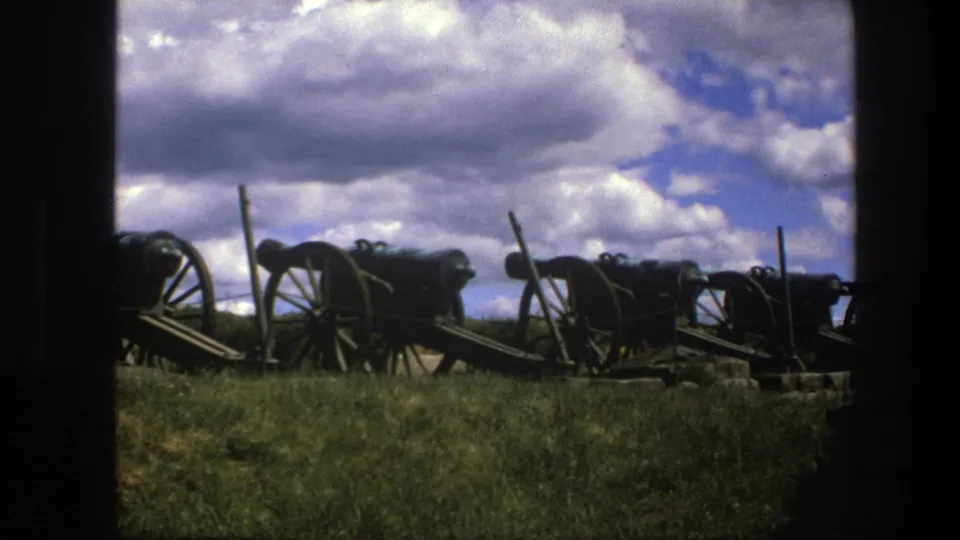 Copenhagen 1975 8mm frame showing several antique cannons in a row, partly framed by dark edges, with grass and dramatic clouds.